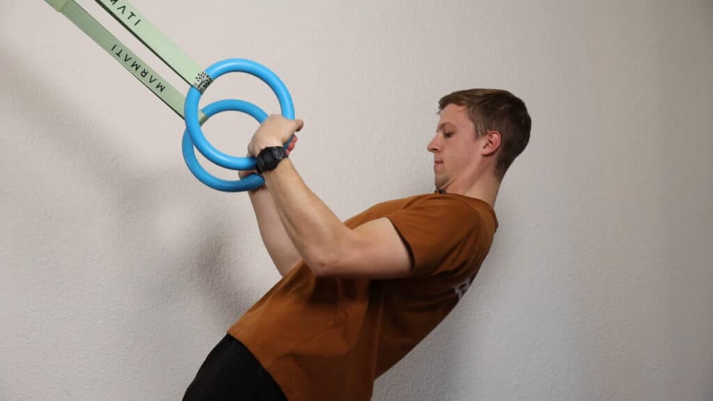 Man in orange shirt performing body rows on the Infinity Rings.