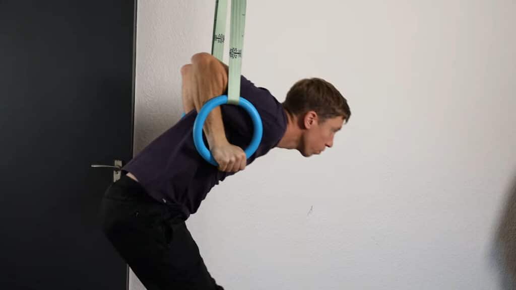 Man in purple shirt performing a Muscle-Up on the Infinity Rings.