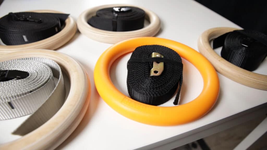 One of the Nayoya Gymnastic Rings amidst other wooden Gymnastic Rings, showing its striking yellow, plastic color.