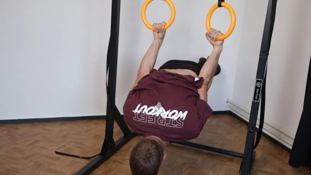 Man in purple shirt performing a back lever on the Nayoya Gymnastic Rings.
