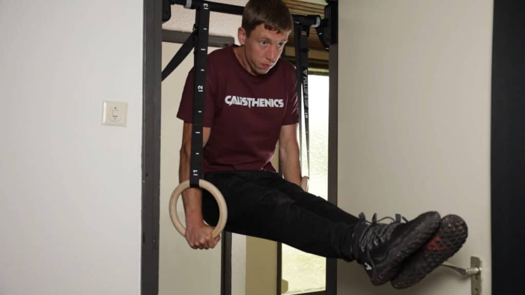 Man in purple shirt performing an L Sit on the Pullup & Dip Gymnastic Rings in a doorway.