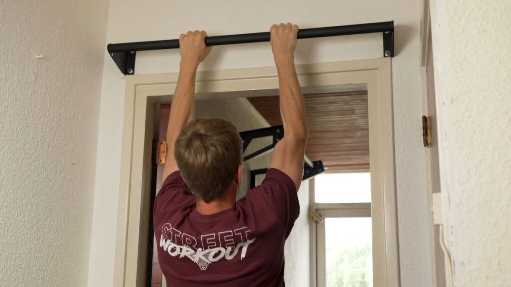 Man hanging from a Pullup & Dip Wall-Mounted Door Pull-Up Bar as his home Pull-Up Bar.