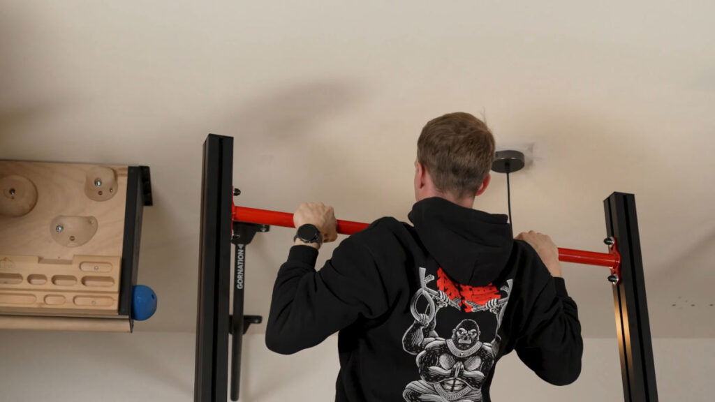 Man in black hoody performing a pull-up on the FitnessKit Basic Strength Bar.