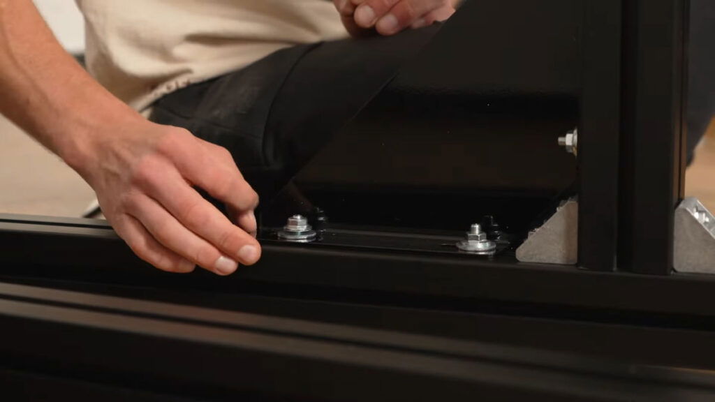 Close up of the assembly of the FitnessKit Basic Strength Bar, a man securing a diagonal sway brace.