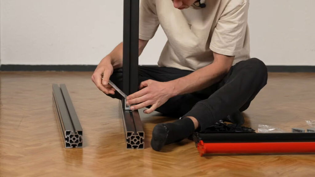Man assembling the FitnessKit Basic Strength Bar by fastening a vertical beam to a floor beam with a elbow joint.