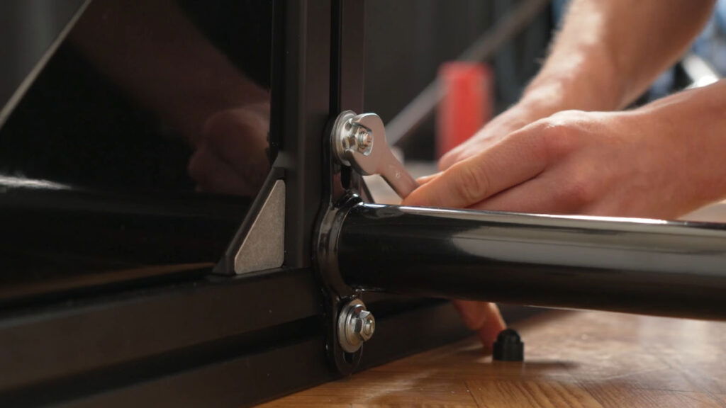 Close up of the FitnessKit Basic Strength Bar bottom bar assembly, with a man fastening one of the nuts.