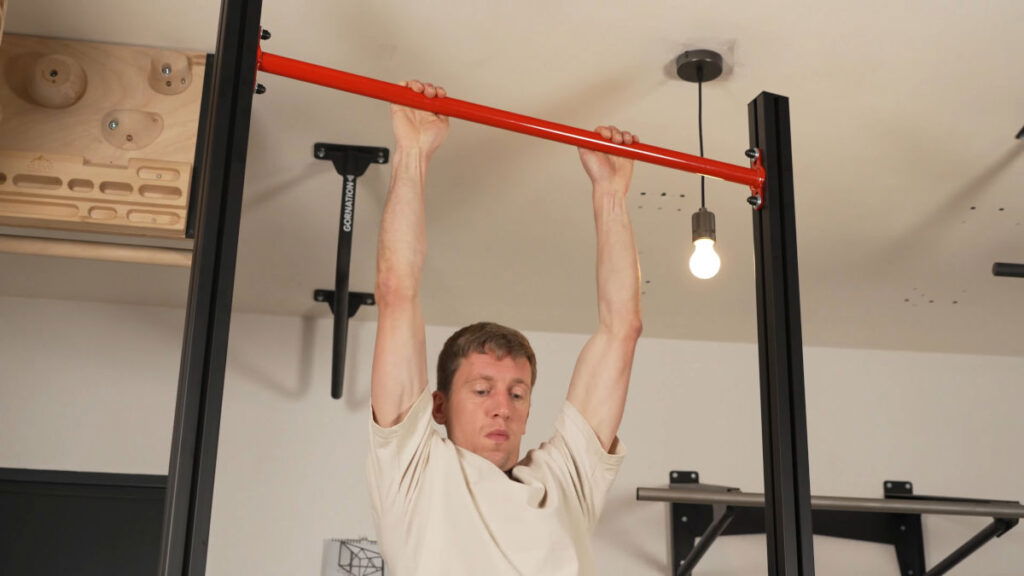 Man in beige shirt performing a pull-up on the FitnessKit Basic Strength Bar.