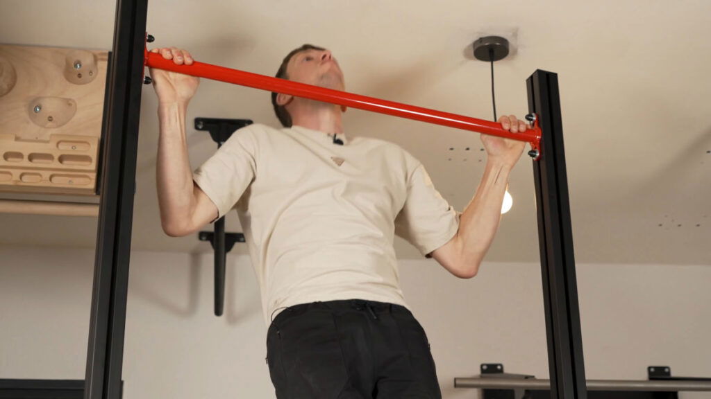 Man in beige shirt performing wide pull-ups on a FitnessKit Basic Strength Bar.