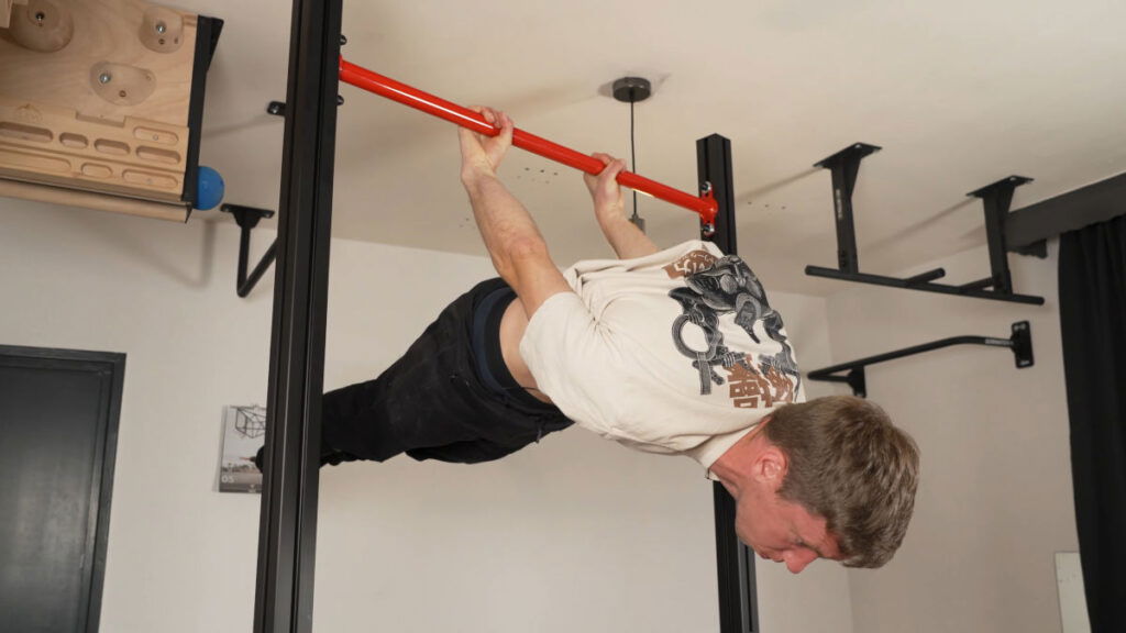 Man in beige shirt performing a back lever on the FitnessKit Basic Strength Bar.