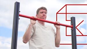 Man in white shirt hanging from a FitnessKit Basic Strength Bar and looking incredulously at the viewer.