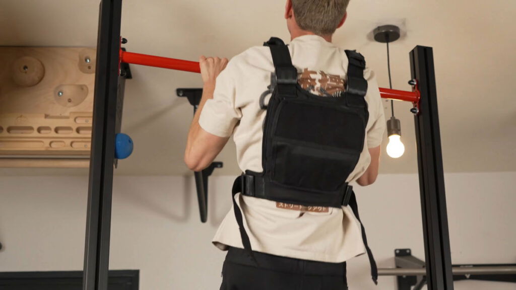 Man wearing a weighted vest performing pull-ups on a FitnessKit Basic Strength Bar.