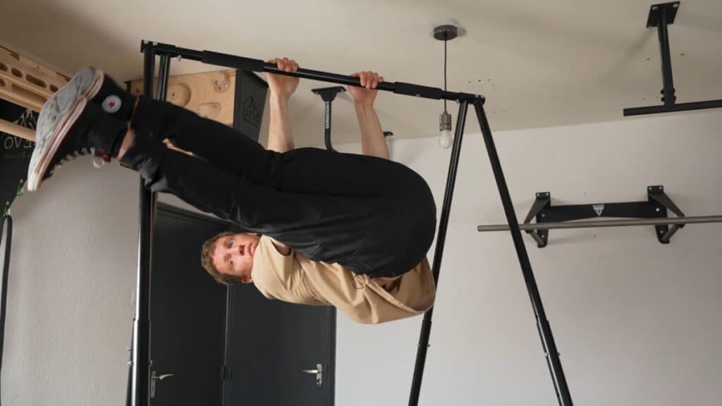 Man wearing black trousers and black vans doing windshield wipers on the Khanh Trinh Pull-Up Bar.