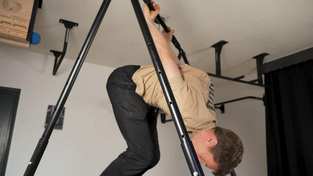 Man in beige shirt completing a skin-the-cat on a Khanh Trinh Pull-Up Bar.