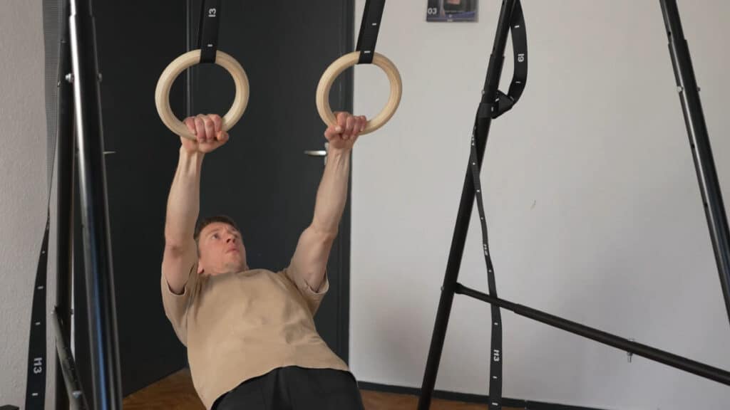Man in beige shirt performing body rows on a set of Gymnastic Rings suspended off a Khanh Trinh Pull-Up Bar.