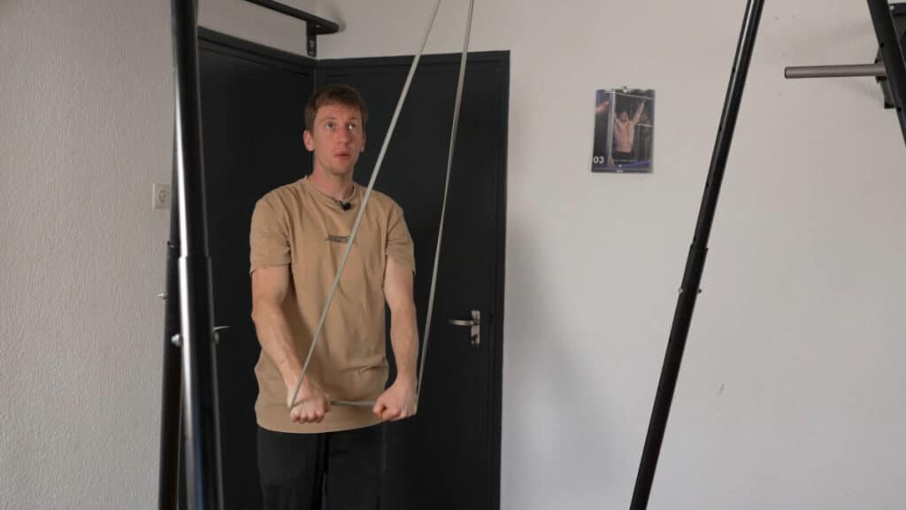 Man in beige shirt performing extensions as a warm up using a Resistance Band suspended from a Khanh Trinh Pull-Up Bar.