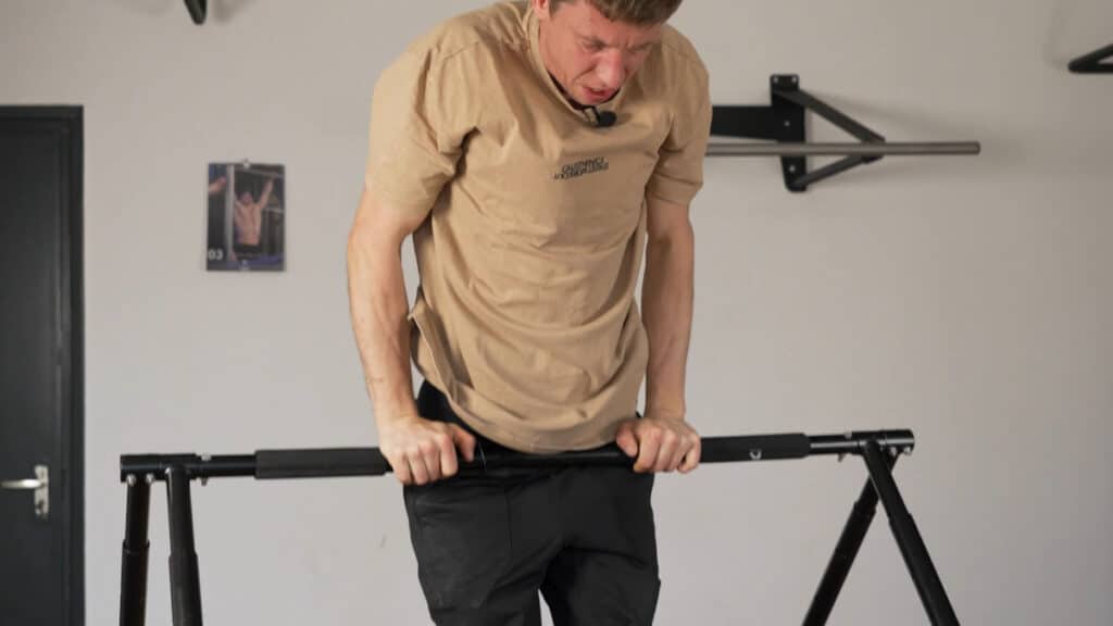 Man in beige shirt doing Straight Bar Dips on a Khanh Trinh Pull-Up Bar in its lowest height setting as a Static Bar.