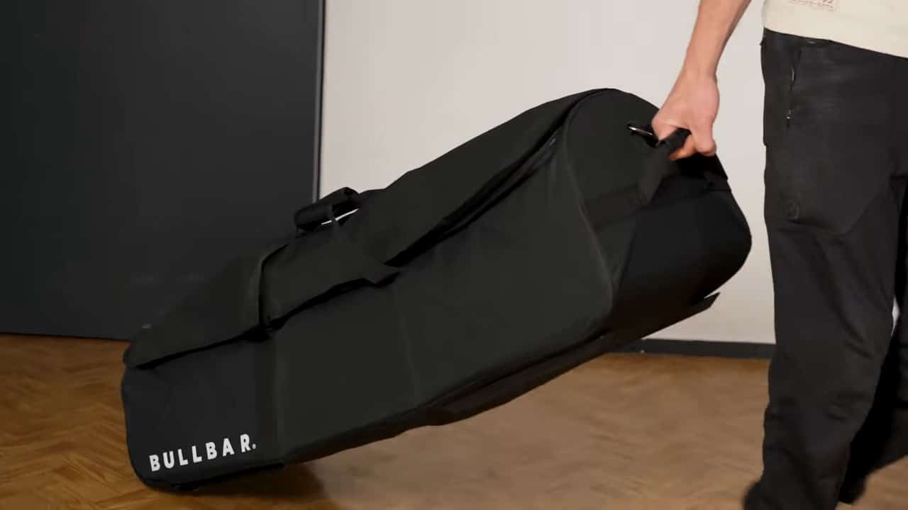 Man dragging the carry bag for the bullbar 2.0 foldable pull-up bar behind him on wheels.