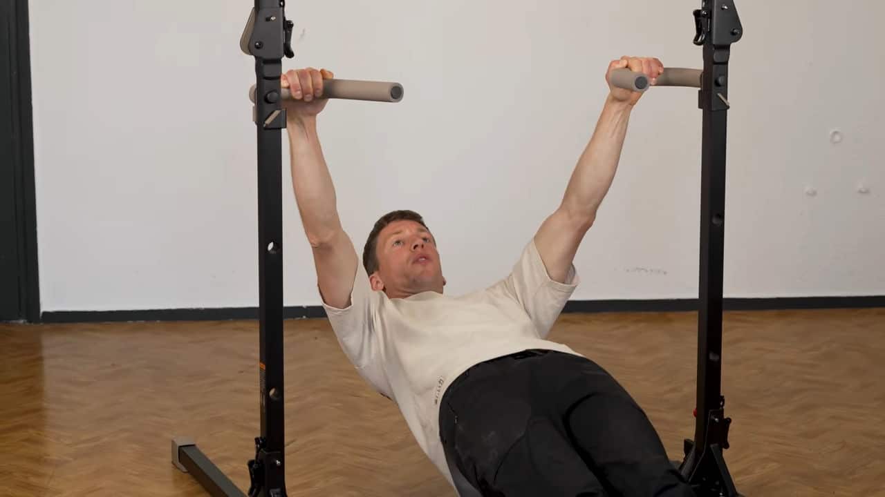 Man in beige shirt doing rows on the dip bars of a bullbar 2.0 foldable pull-up bar.