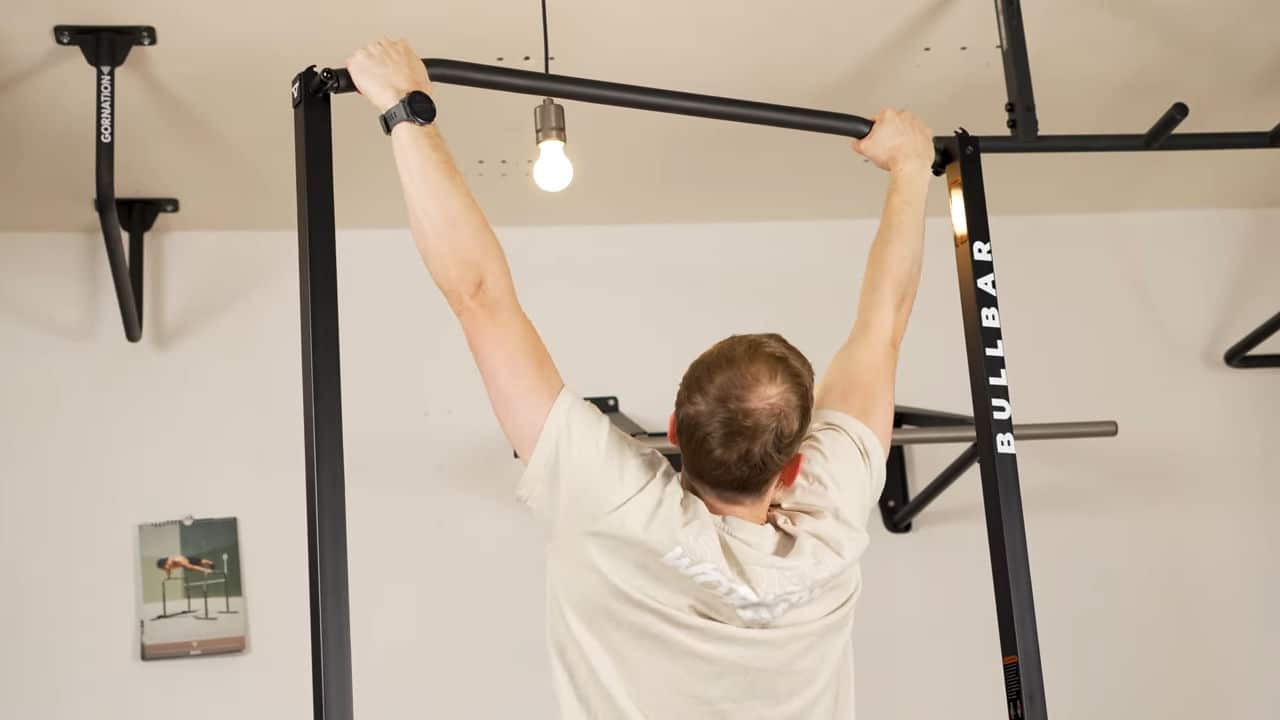 Man in beige shirt using the slanted grips of the bullbar 2.0 foldable pull-up bar.