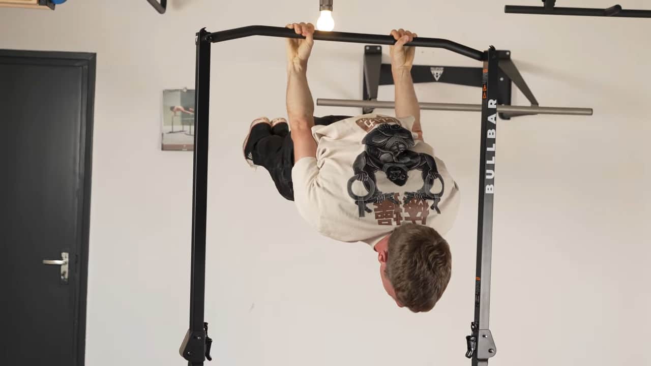 Man in beige shirt with japanese lettering print performing a back lever on the bullbar 2.0 foldable pull-up bar.