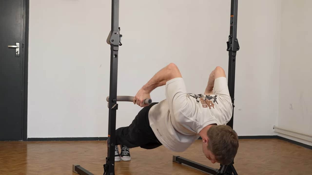 Man in beige shirt doing deep push-ups on the dip bars of a bullbar 2.0 foldable pull-up bar.