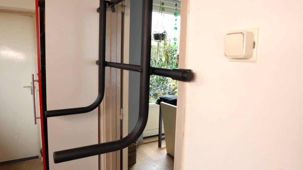 Diagonal front view of the Pullup & Dip Doorway Dip Bar resting against the frame of an opened door.