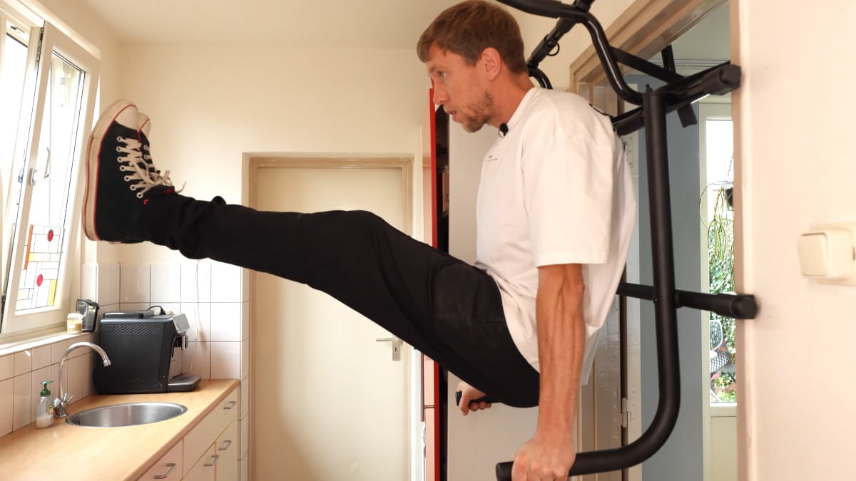 Man in white shirt performing leg raises on the Pullup & Dip Doorway Dip Bar.