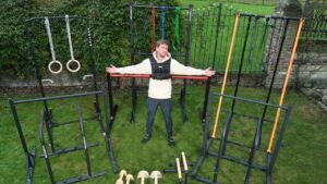 Man standing invitingly between a selection of the best calisthenics equipment while wearing a weighted vest.