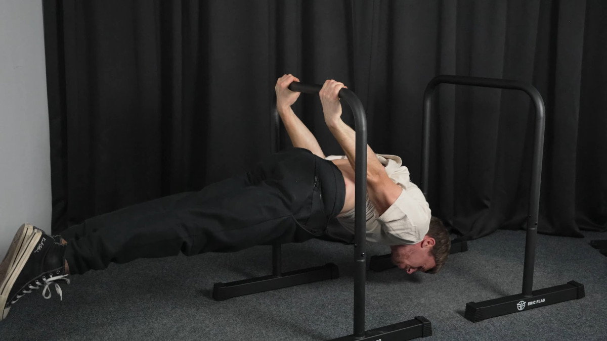 Man in white shirt performing back levers on the eric flag dip bars.