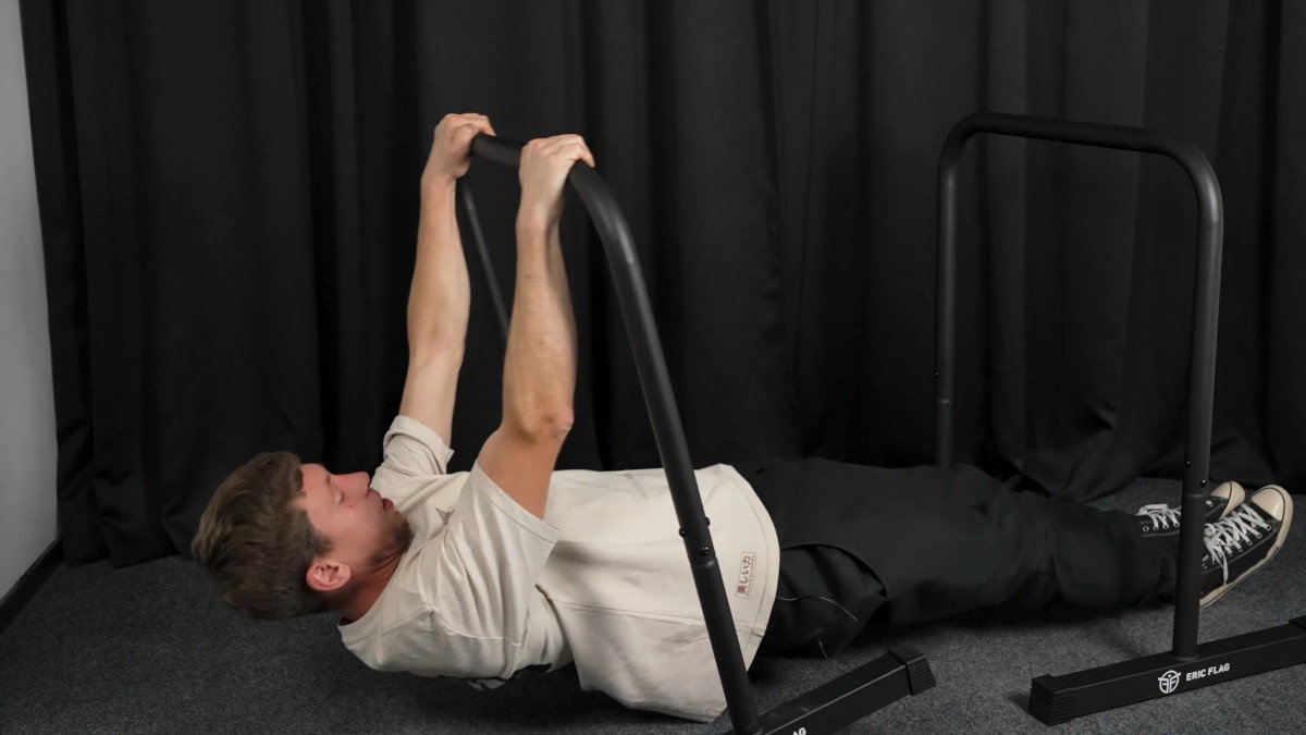 Man in white shirt attempting rows on the eric flag dip bars but failing when the bar tips over.