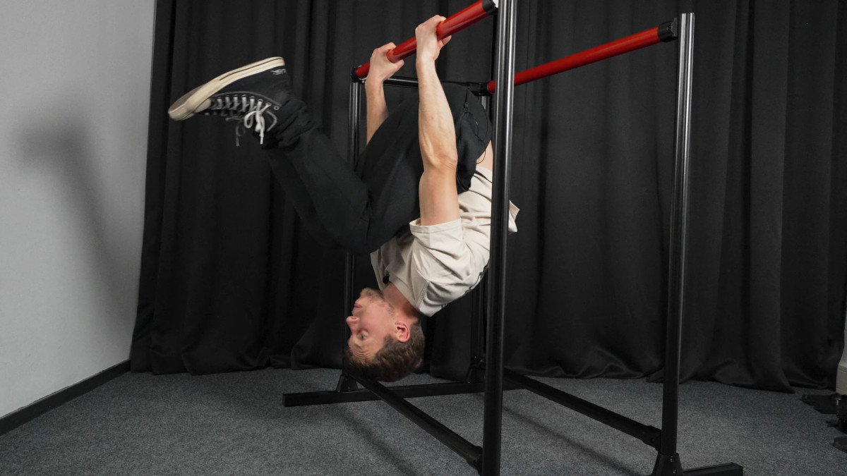 Man in white shirt performing a skin the cat on the fitnesskit dip bars.