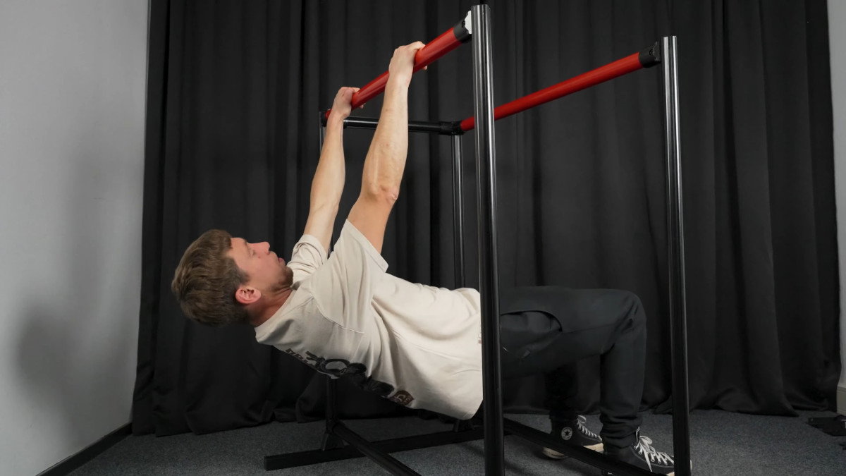 Man in white shirt performing rows with bent knees on the fitnesskit dip bars.