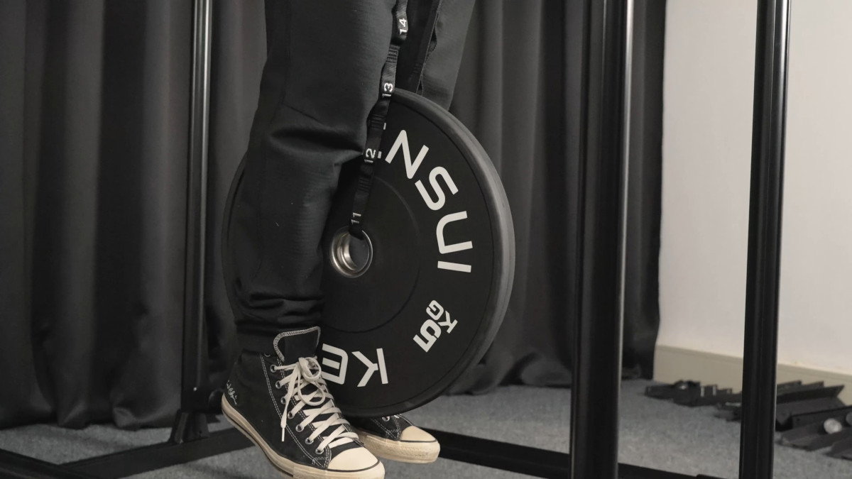 Man performing weighted dips with a dip belt on the fitnesskit dip bars, the large weight plate between his feet.