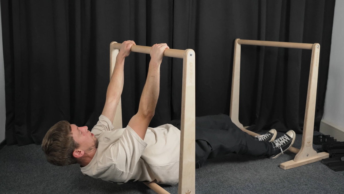 Man in white shirt performing rows on the gorletic wooden dip bars.