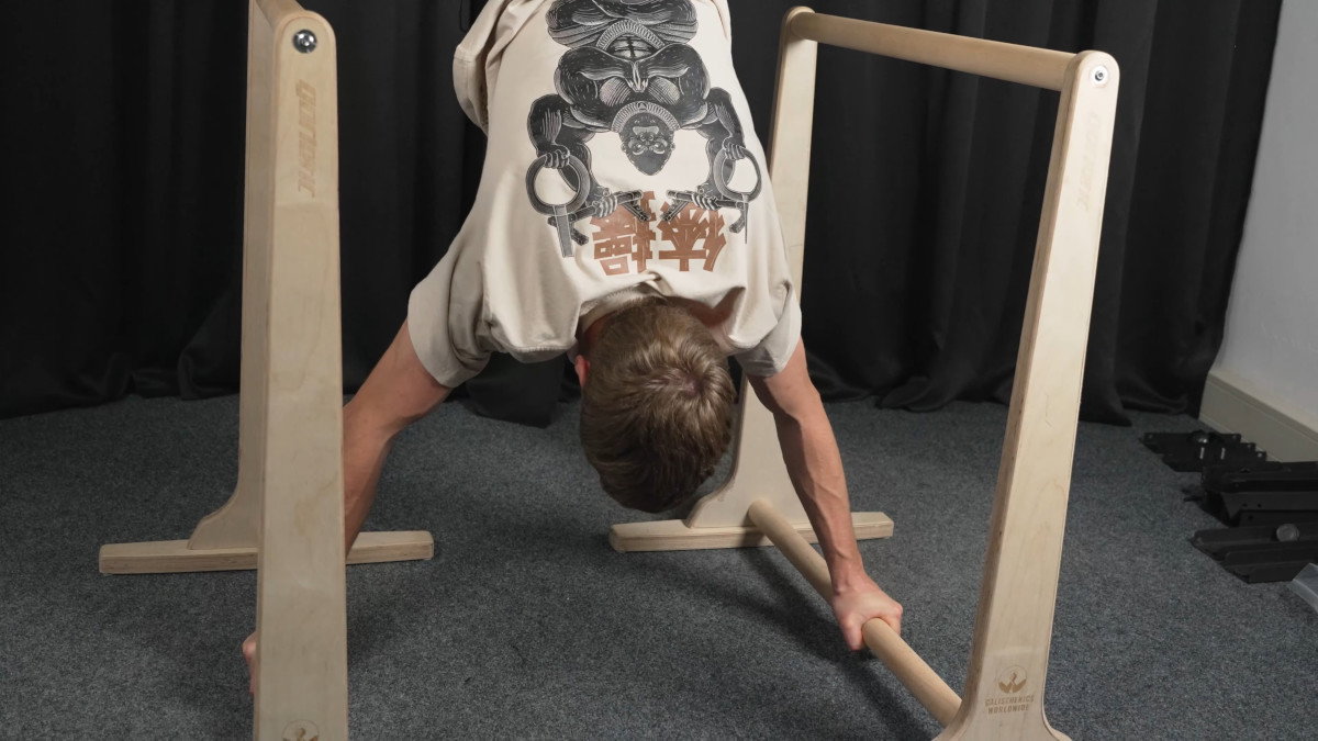Man in white shirt performing handstands on the gorletic wooden dip bars.