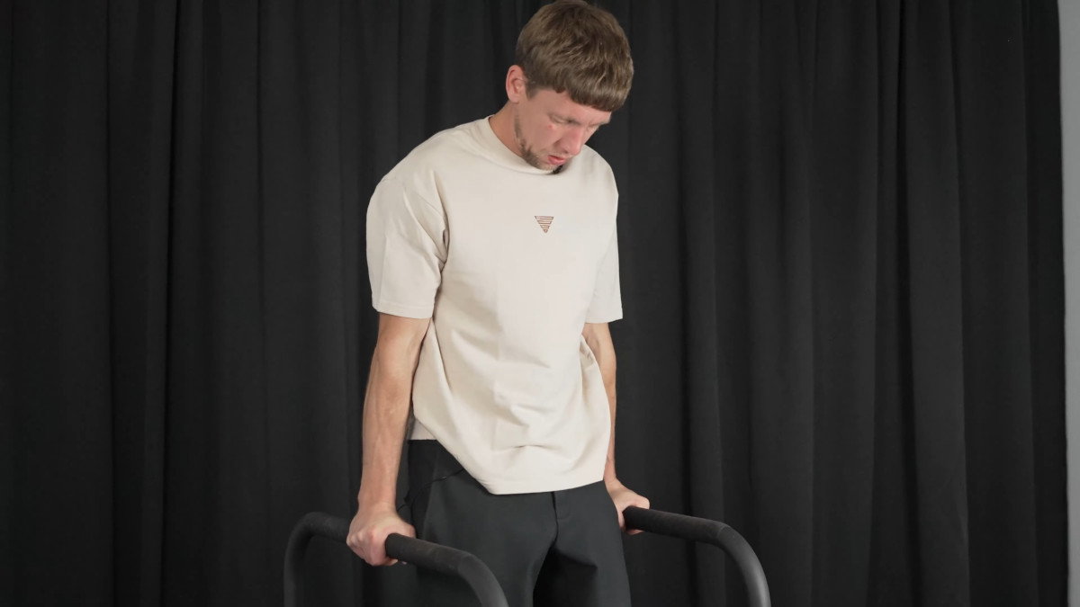 Man in white shirt performing dips on the gornation dip bars.
