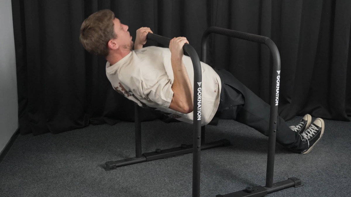 Man in white shirt performing rows on the gornation dip bars.