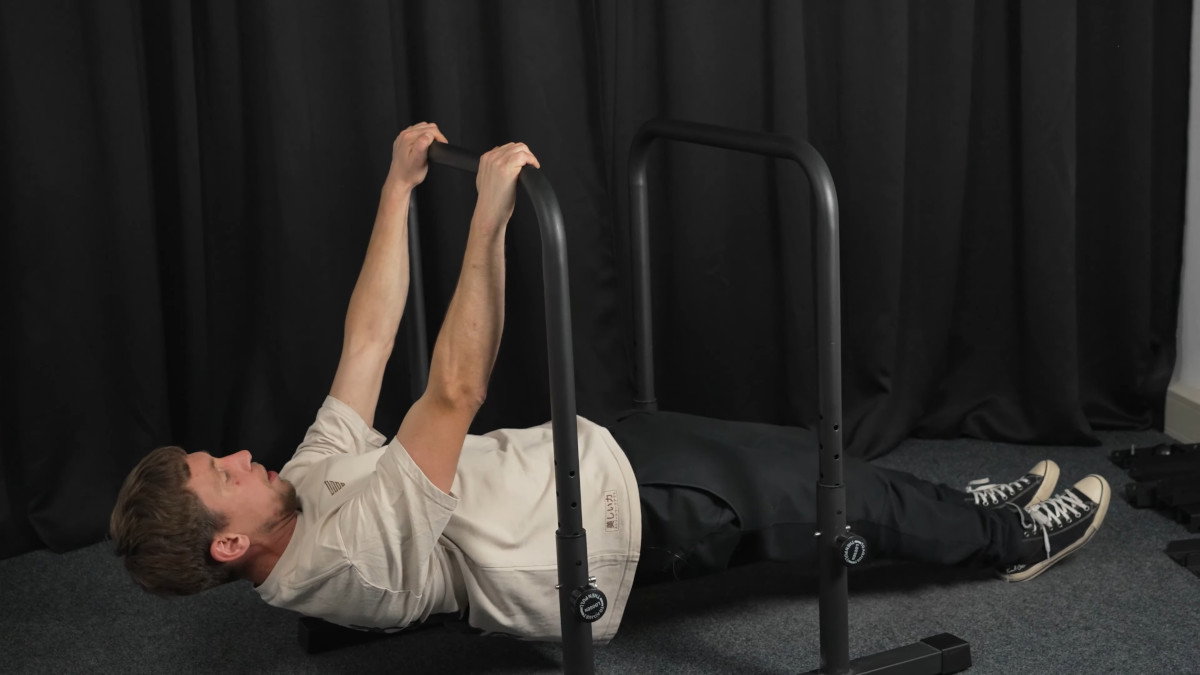 Man in white shirt performing rows on the gravity fitness dip bars.