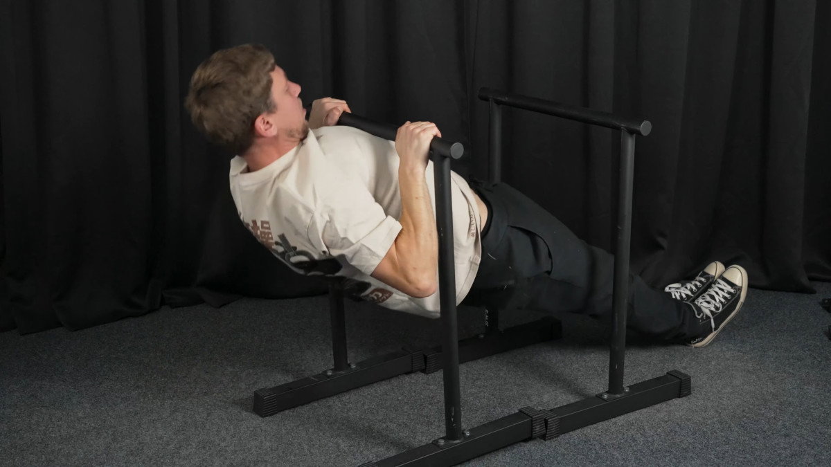 Man in white shirt performing rows on the ramass dip bars.