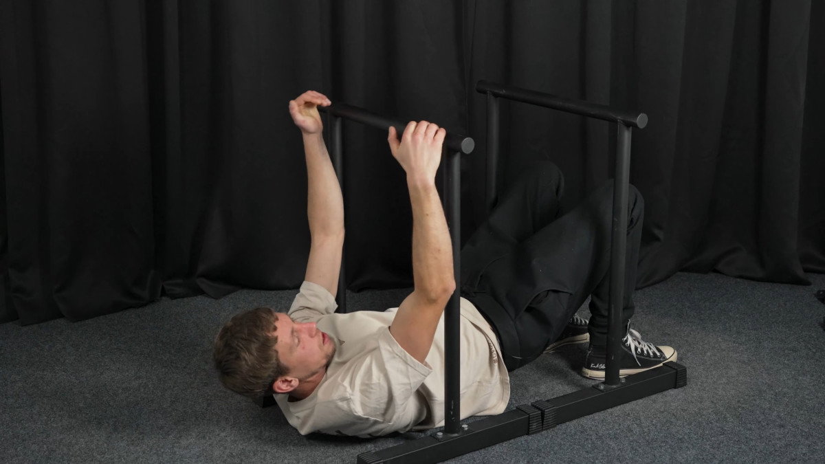 Man in white shirt attempting rows on the ramass dip bars but failing because it is too narrow.