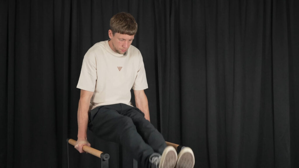 Man in white shirt performing an l-sit on the thenx dip bars.