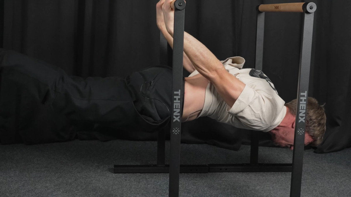 Man in white shirt performing a back lever on the thenx best dip bars.