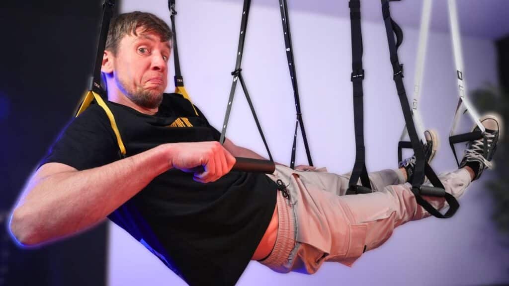 Man in black shirt hangs in the air suspended by many suspension trainers and looking questionable at the viewer.