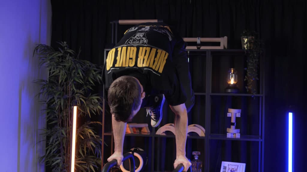 Man performing a tucked handstand on the eric flag dip bars.