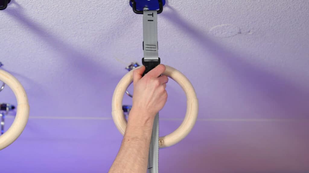 A man's hand fastening the Marmati Gymnastic Rings with a slide-and-click system at the desired height.