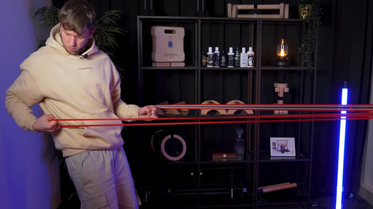 Man in beige hoodie comparing latex and fabric resistance bands, the latex bands being considerably more stretchy.