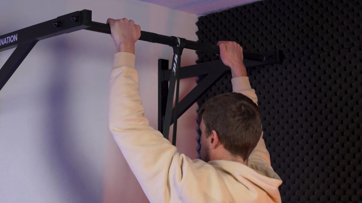 Man in beige hoody doing assisted pull-ups with a gorletic resistance band.