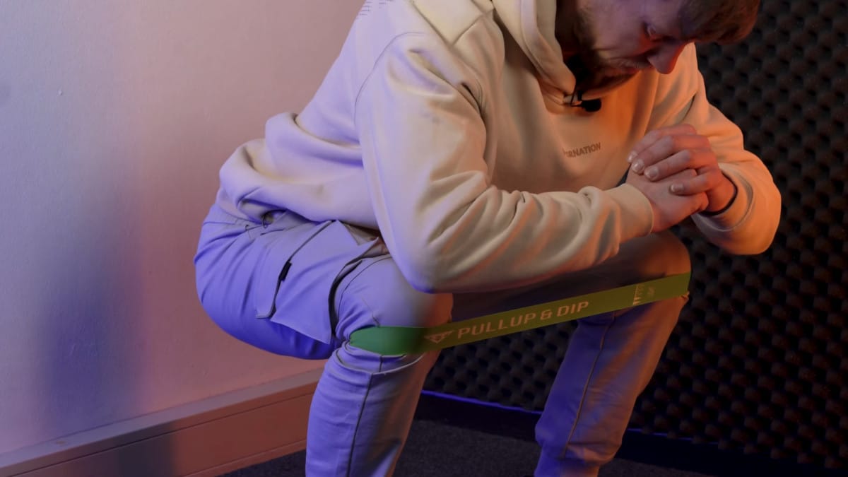 Man doing banded squats with a pullup & dip booty band.