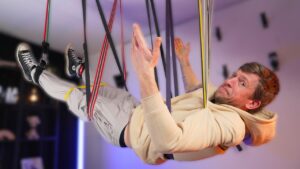 Man hanging freely by a large number of resistance bands and looking doubtfully at the camera.