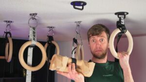 Man standing in a compact home gym consisting of ceiling hooks, gymnastic rings, straps and parallettes.